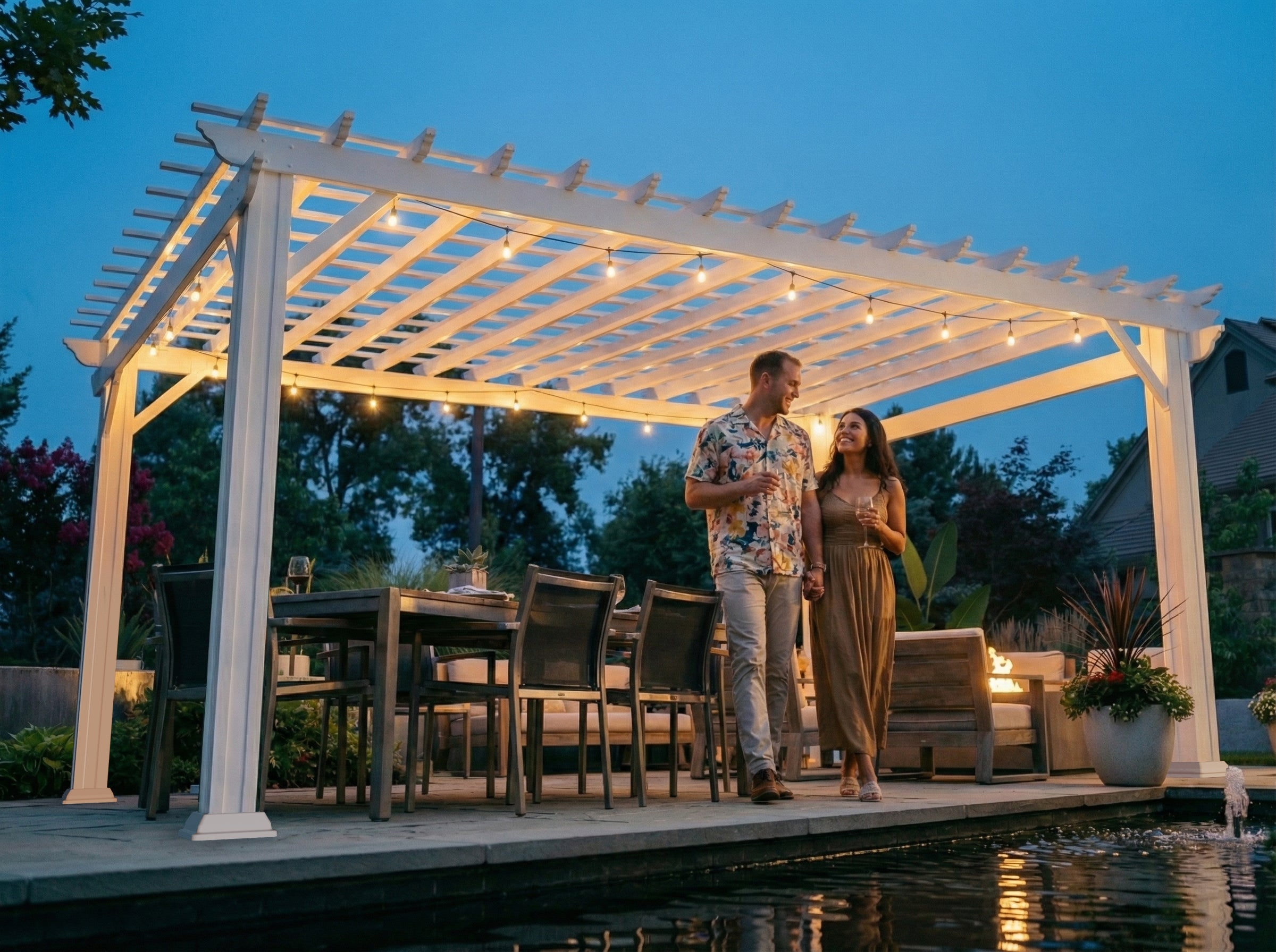 White Stratford modern pergola with trellis roof and string lights over waterfront dining area with couple and fire feature.