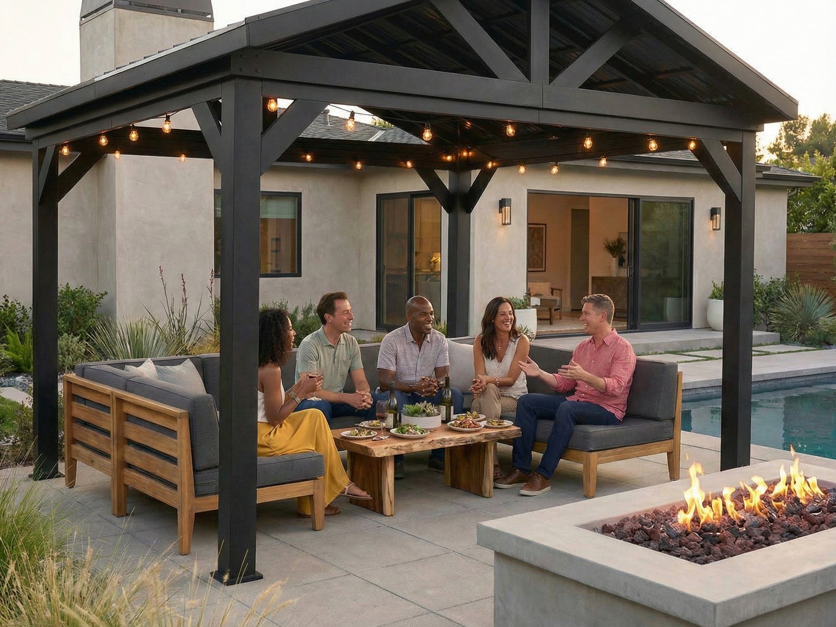 Lancaster steel gazebo with gabled roof and string lights sheltering outdoor seating area beside fire pit and pool.