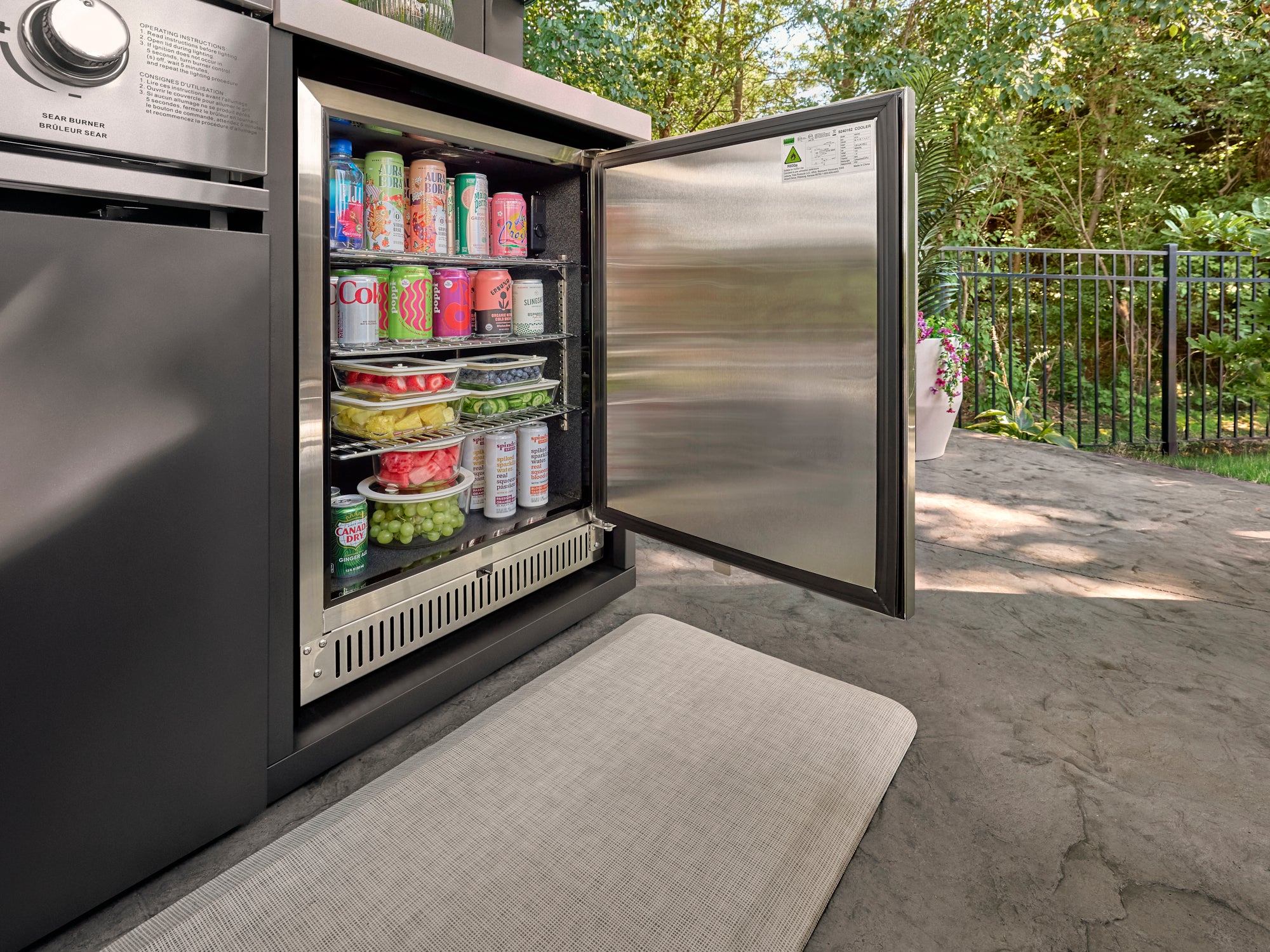 Open outdoor refrigerator revealing three-tier storage in stainless steel on patio kitchen.