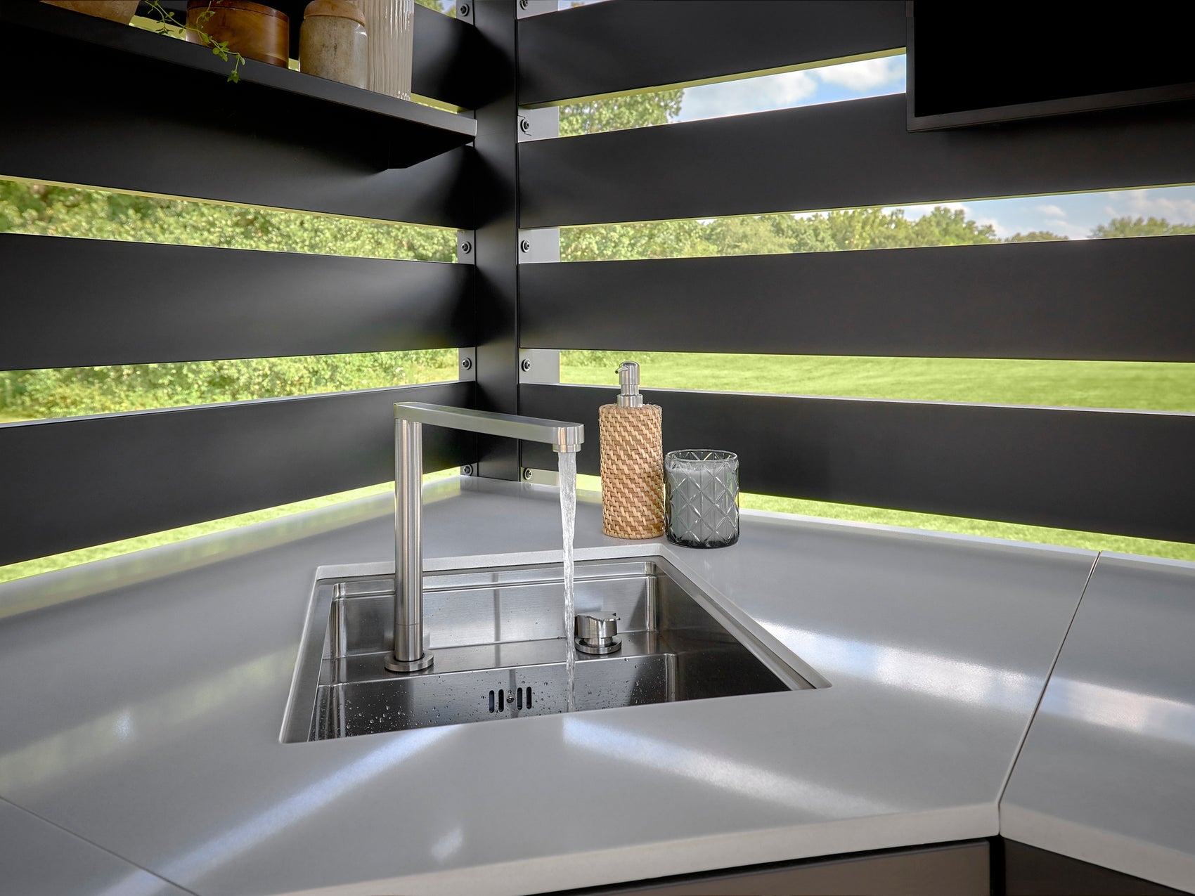 Built-in sink with modern faucet on engineered stone countertop with horizontal slat privacy wall and garden view.