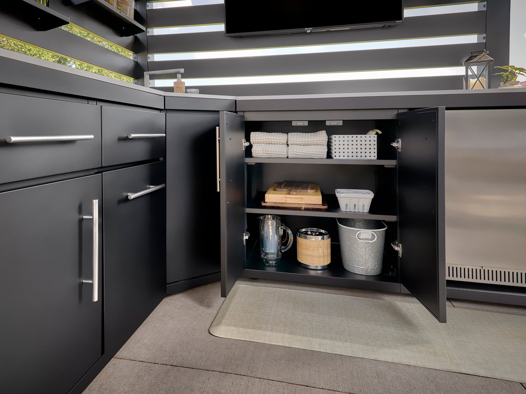 Langston open outdoor kitchen storage cabinet with three shelves holding towels, containers, pitcher, and metal bins.