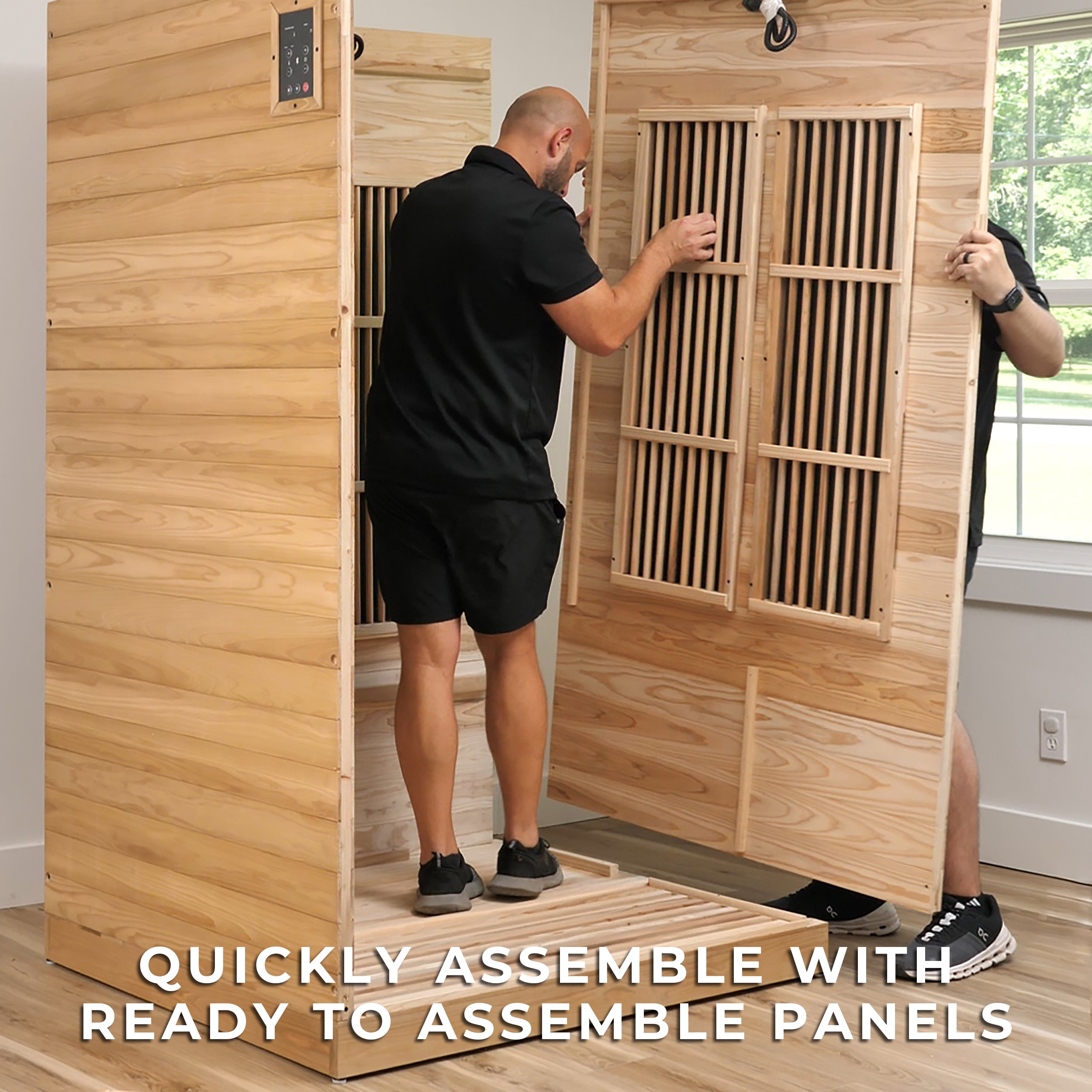 DIY assembly of indoor cedar Rylan sauna kit showing person installing pre-fabricated wall panels with infrared heaters