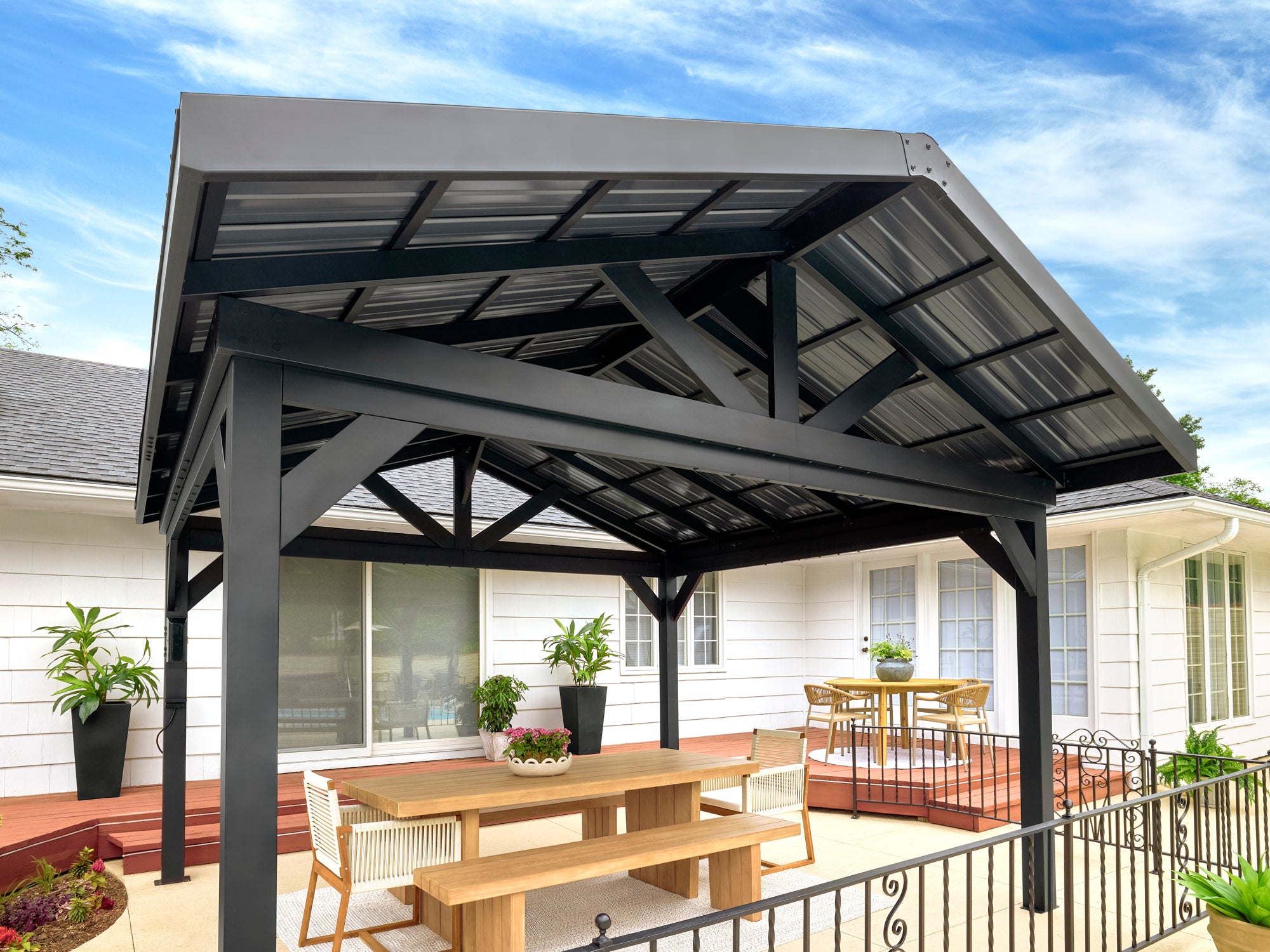 Steel gable roof gazebo with metal hardtop on wooden deck, furnished with dining table for outdoor entertaining.