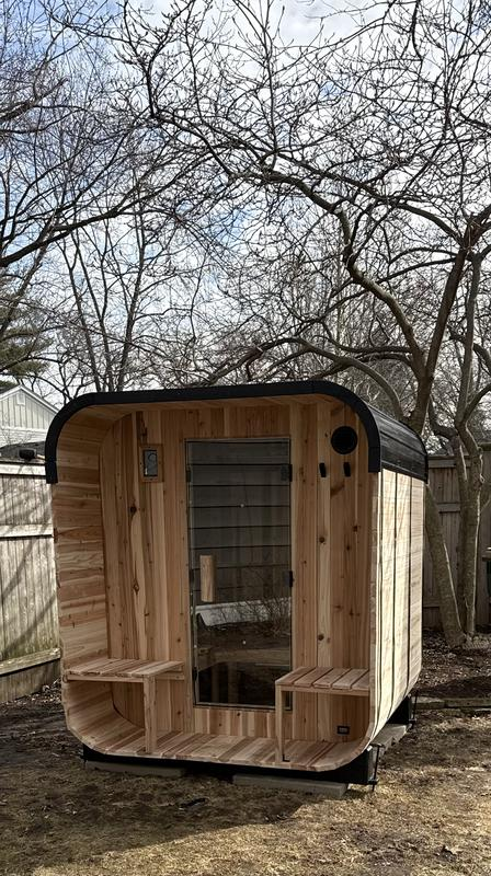 Wooden cabin-style shed with a curved front design in a backyard setting.