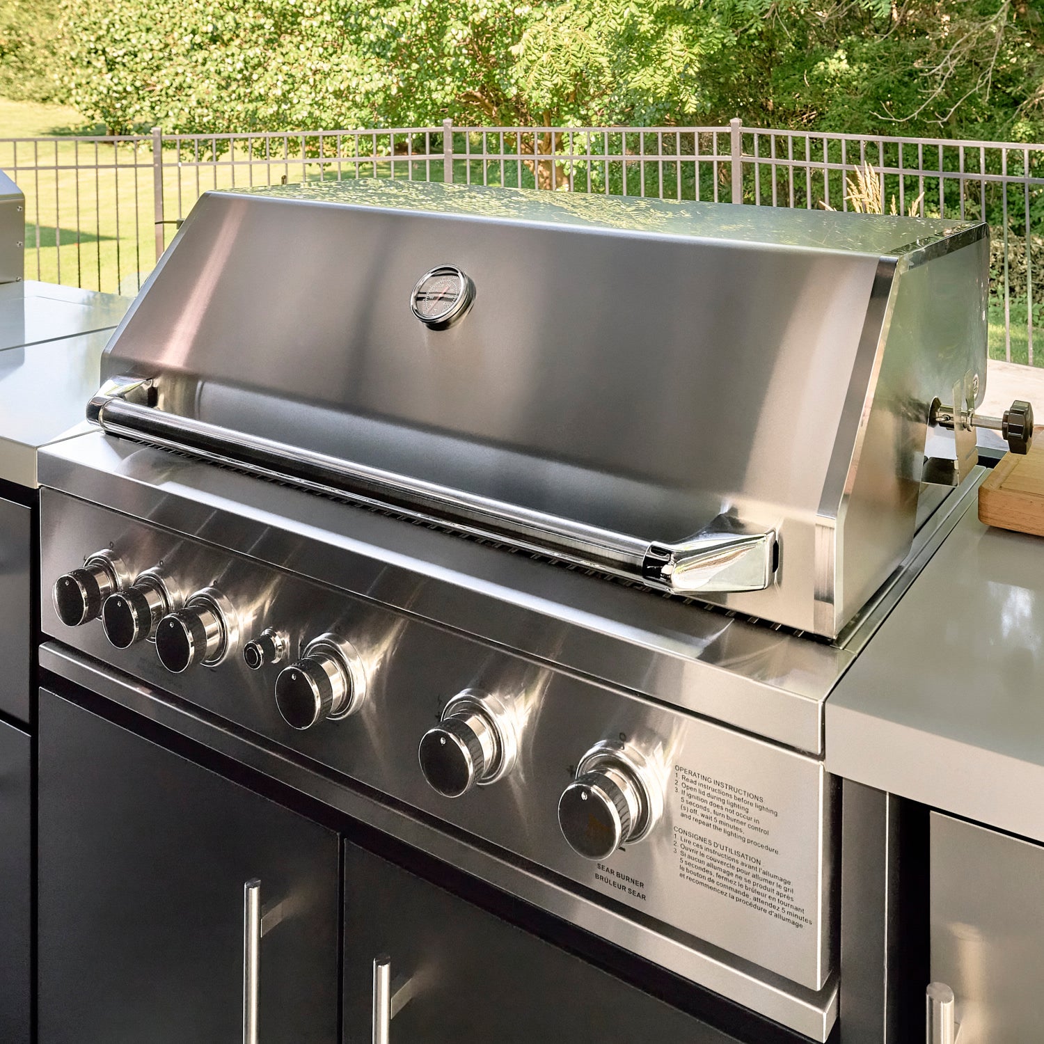 Built-in stainless steel grill with five burners on covered outdoor kitchen island at sunset