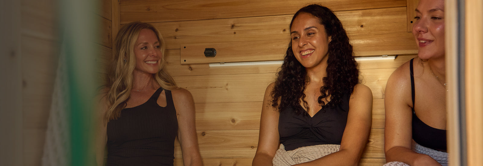 Three women sitting together in a wooden sauna.