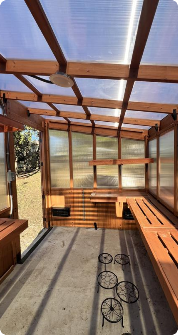Wooden structure with transparent roof and walls, possibly a greenhouse or sunroom.