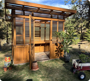 Cedar greenhouse with a 4-wall polycarbonate roof in a garden setting.