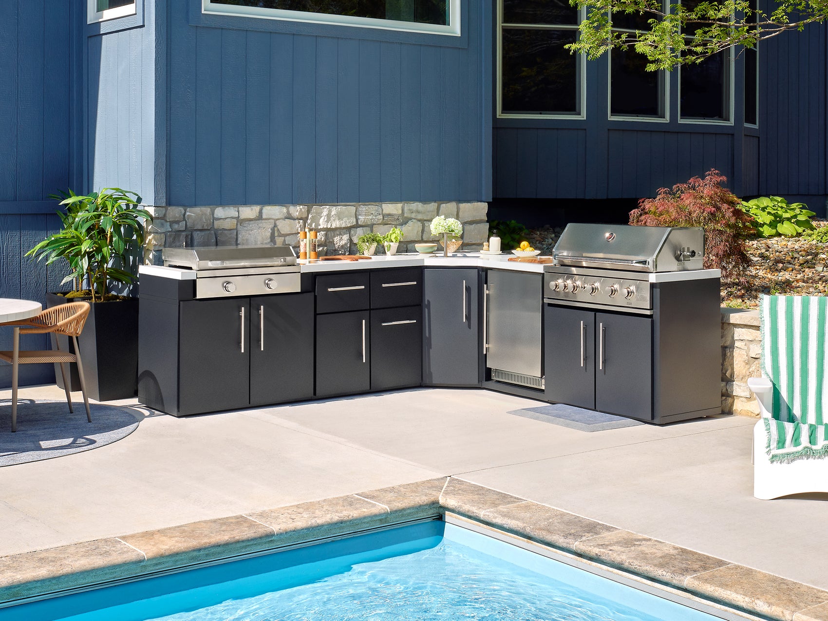 Poolside Emory L-shaped outdoor kitchen features a griddle grill combo and engineered stone countertops.