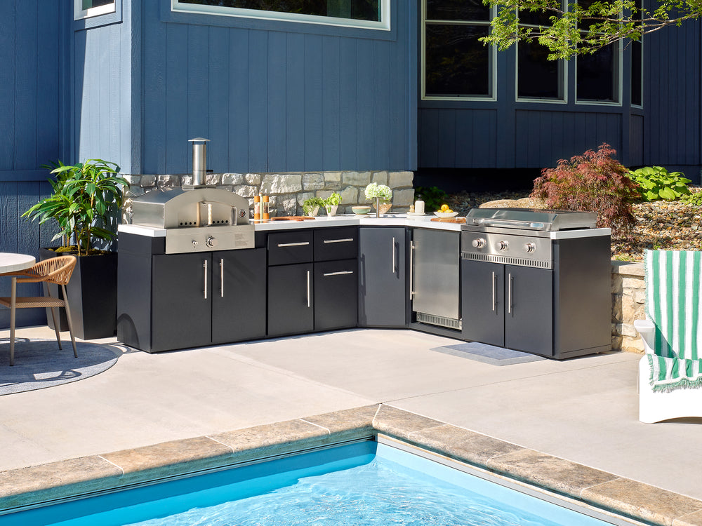 L-shaped Emory outdoor kitchen with a pizza oven, grill, and galvanized steel cabinets by a pool.