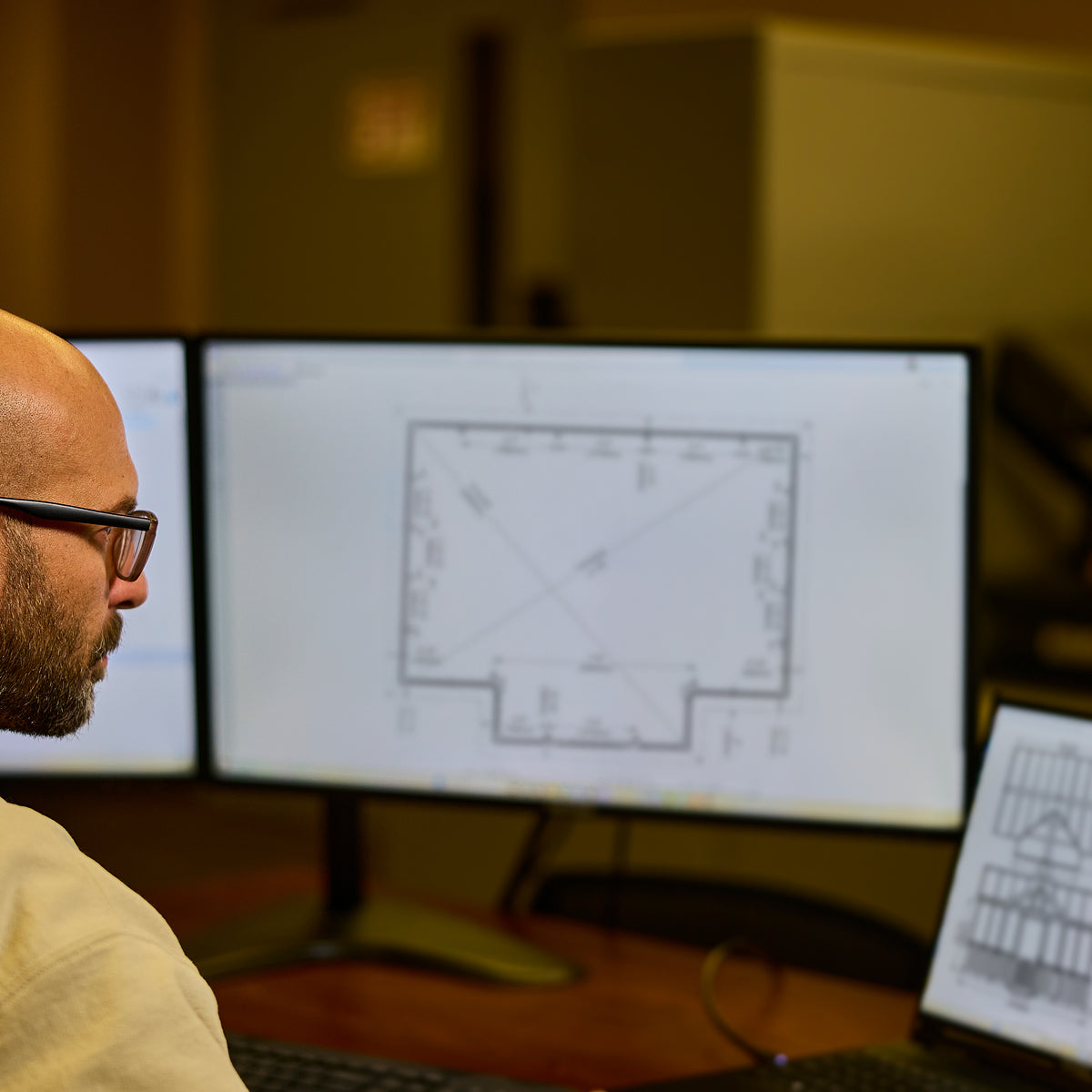 Engineer reviewing structural drawings for a greenhouse kit on multiple computer monitors.