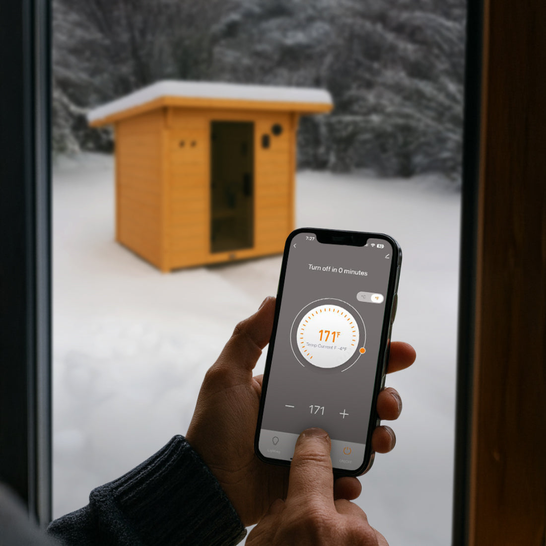 Person inside using Tuya Smart App on smartphone to control Henley Outdoor Sauna temperature in a snowy outdoor setting