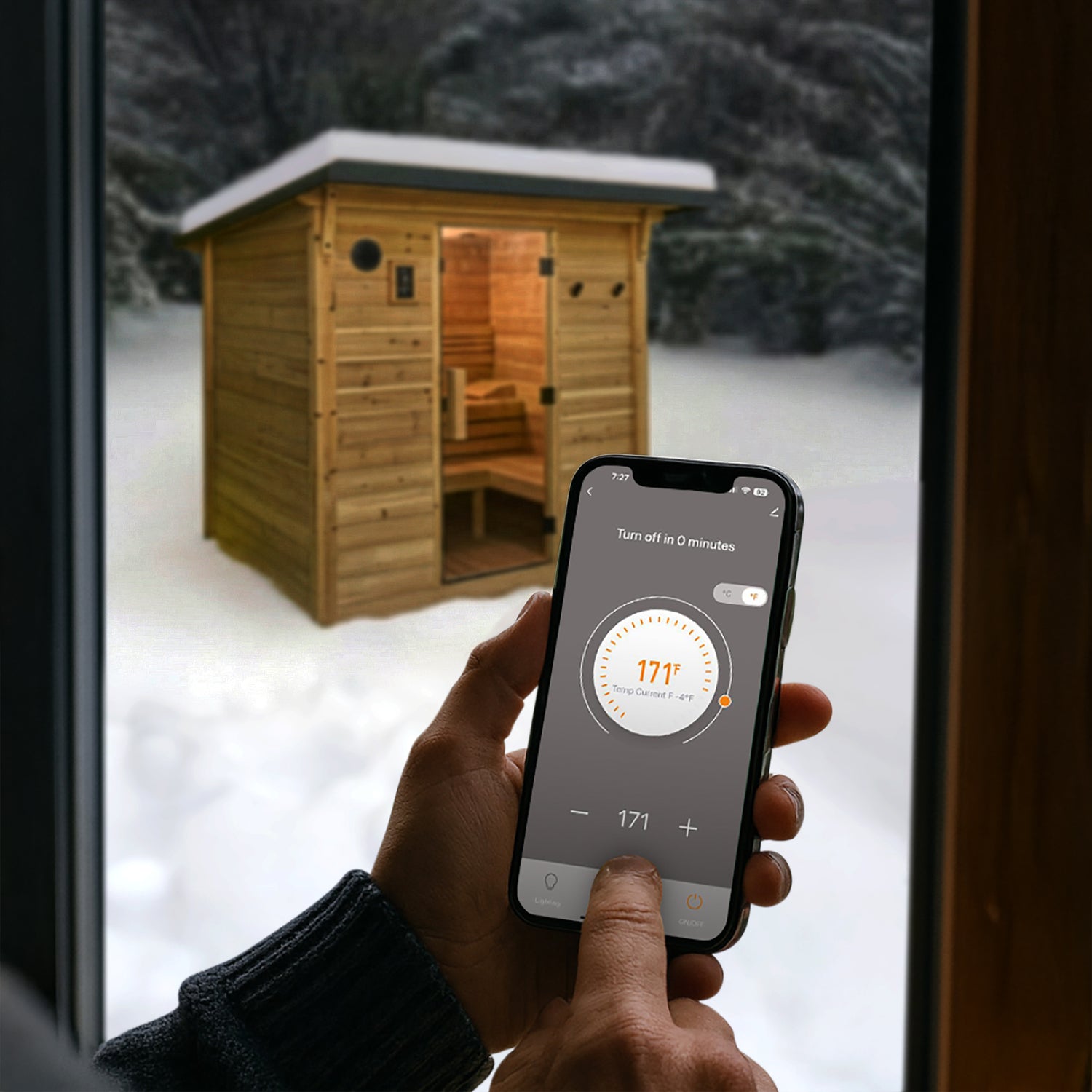 Person inside using Tuya Smart App on smartphone to control Henley Outdoor Sauna temperature in a snowy outdoor setting