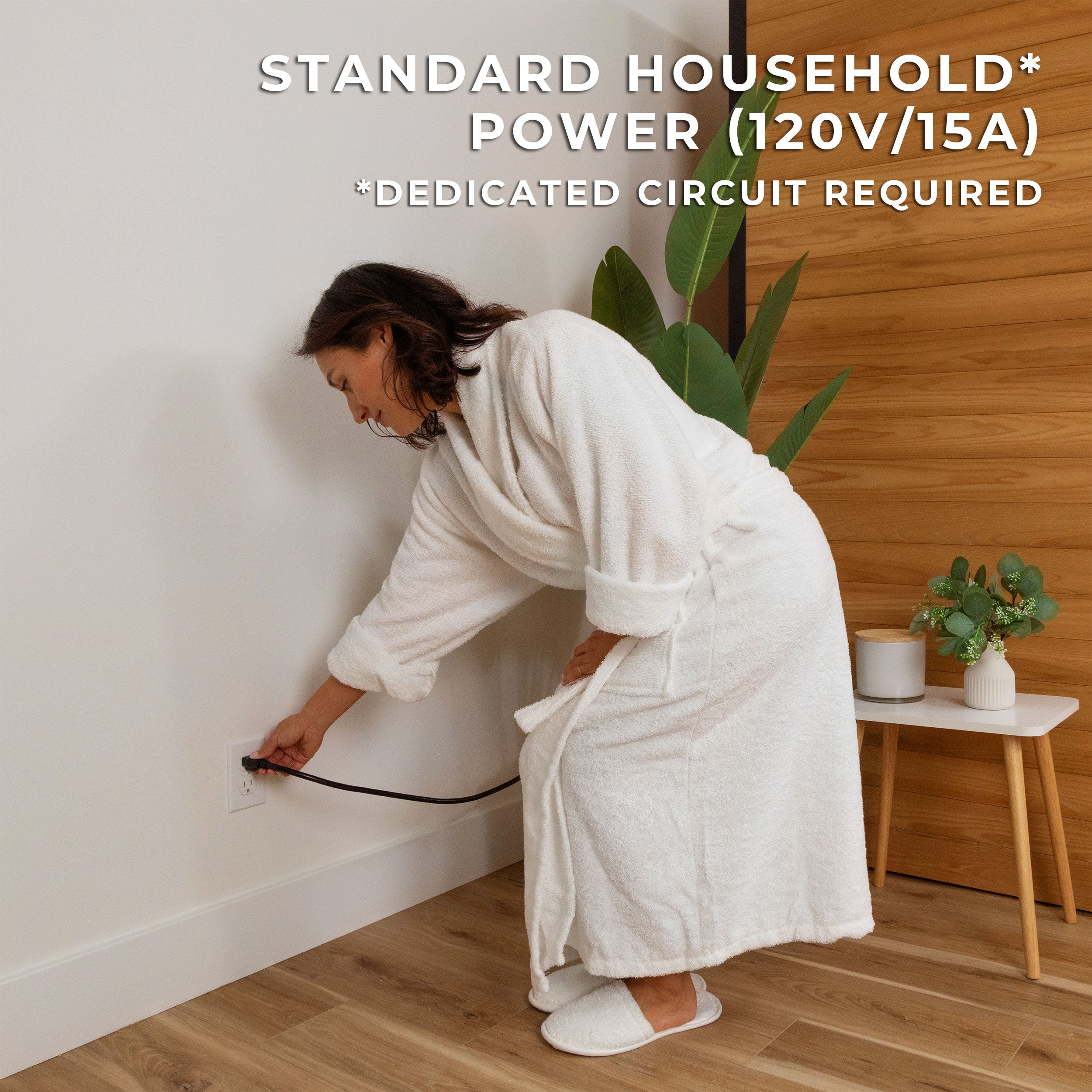 Woman in white robe plugging Rylan infrared sauna into standard wall outlet for easy setup