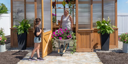 Two women standing in a greenhouse with plants and gardening tools.