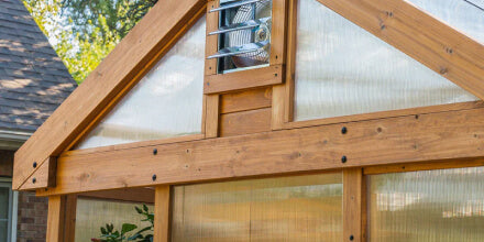 Cedar wooden framed greenhouse with polycarbonate panels in a backyard setting.