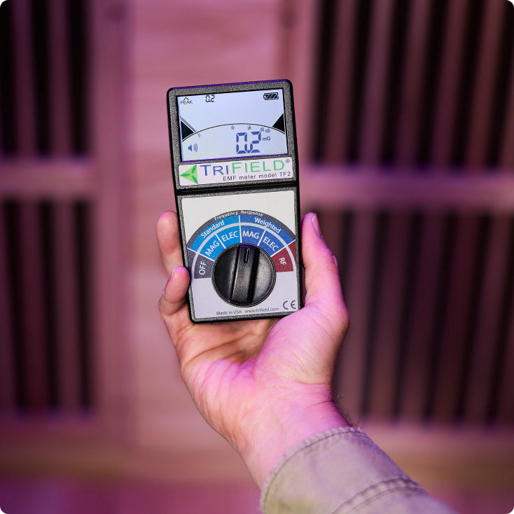 Hand holding a Trifield EMF meter against a blurred background