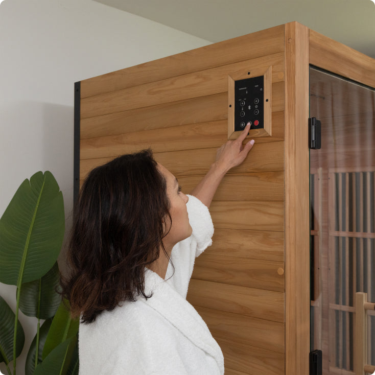 Woman in a white robe adjusting controls on a wooden sauna.