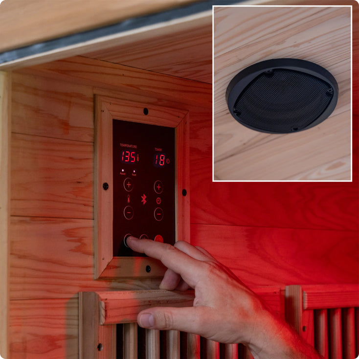Hand adjusting a digital control panel on a wooden sauna with a close-up of a speaker.