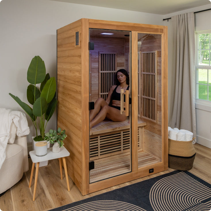 Person sitting inside a wooden infrared sauna in a home setting.