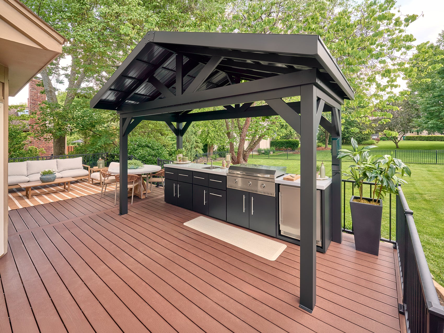 Lancaster Linear outdoor kitchen with a stainless steel grill and galvanized steel roof on a backyard wood deck.
