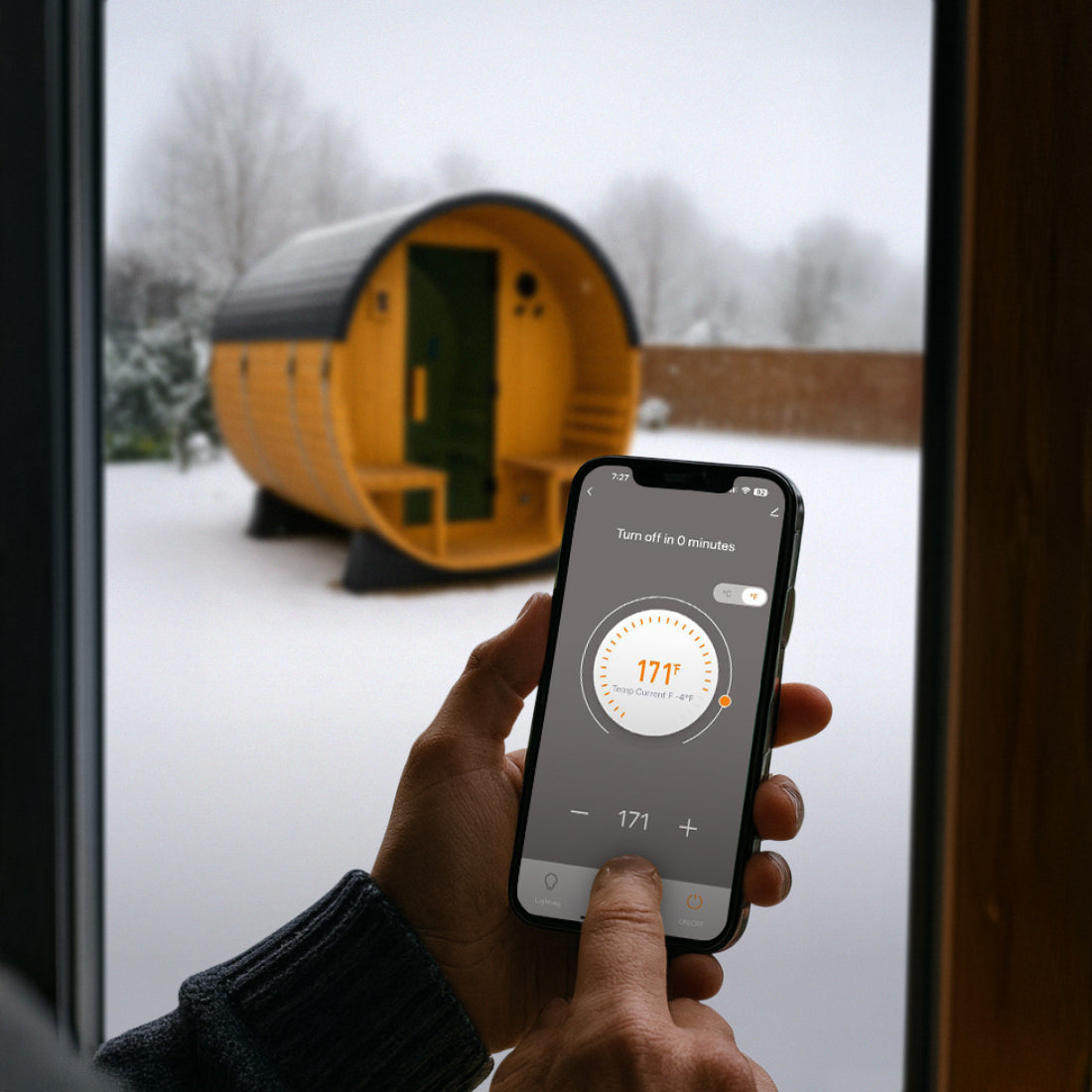 Person inside using Tuya Smart App on smartphone to control Paxton Outdoor Sauna temperature in a snowy outdoor setting