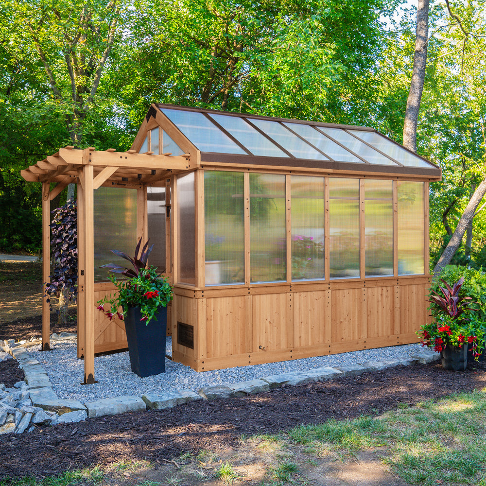 Bellerose cedar-frame greenhouse shed with polycarbonate panels set in a landscaped backyard with colorful plants.