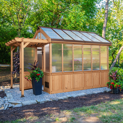 Bellerose cedar-frame greenhouse shed with polycarbonate panels set in a landscaped backyard with colorful plants.