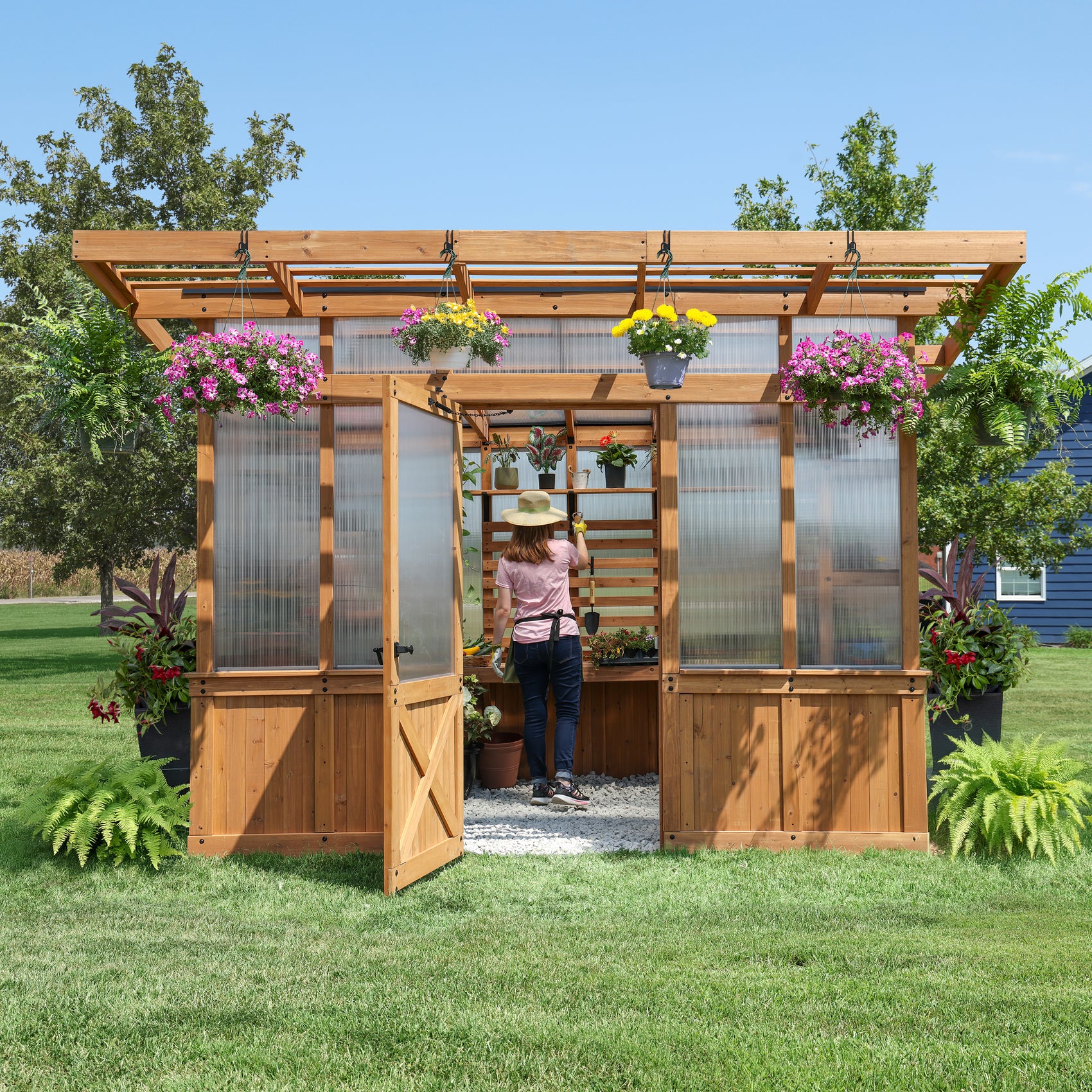 Woman tending plants inside the 11x7 Poppy cedar and polycarbonate greenhouse with an integrated pergola overhang.