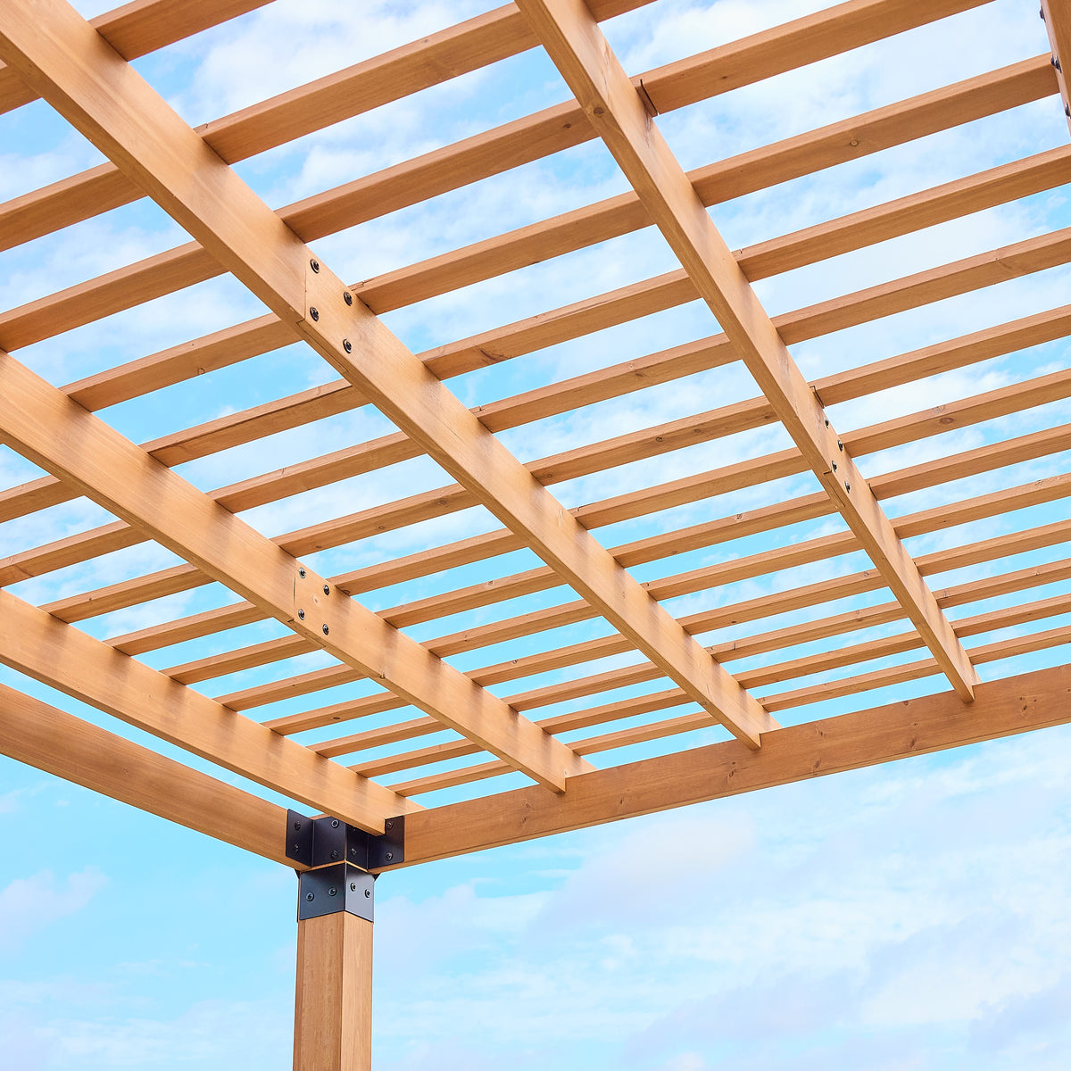 Slatted pergola roof of open cedar crossbeams filtering sunlight against a bright blue sky.