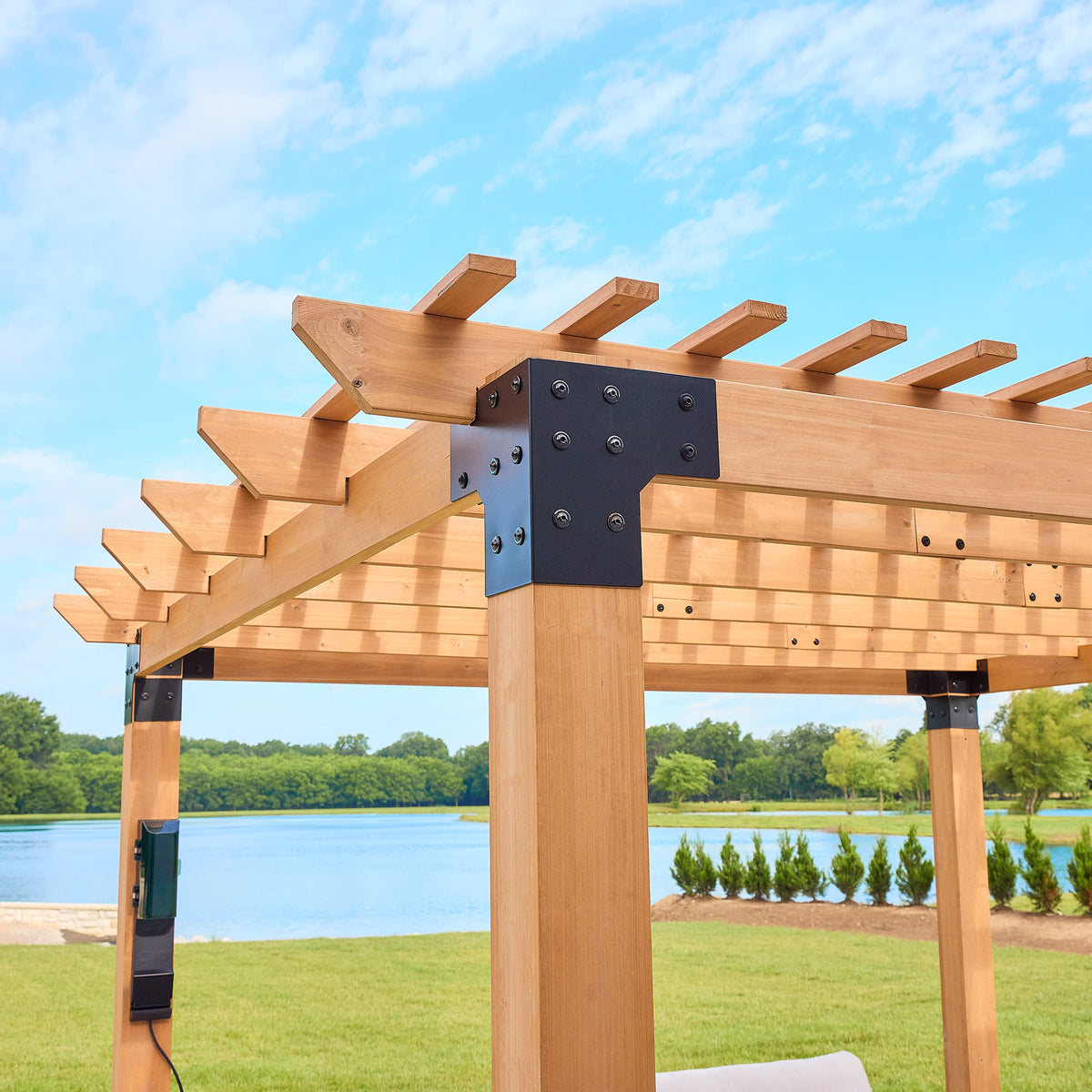 Thick cedar posts anchoring the beams and open slat roof of a freestanding wood pergola.