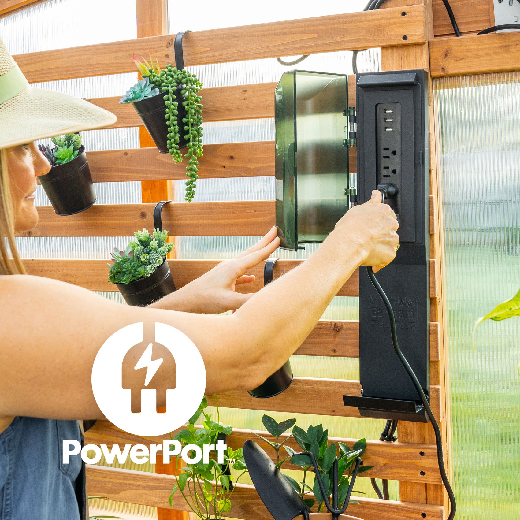 Woman opening the weatherproof PowerPort electric hub with 3 outlets and 3 USB ports on the walk-in greenhouse wall.