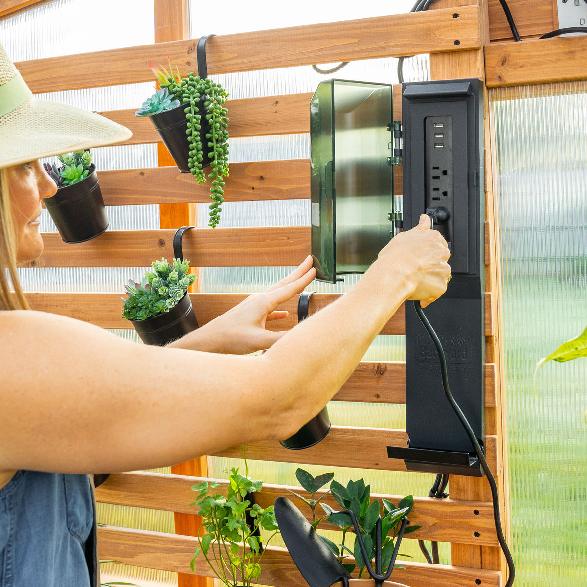 Woman plugging into a PowerPort hub mounted on a cedar slat wall inside a greenhouse kit.