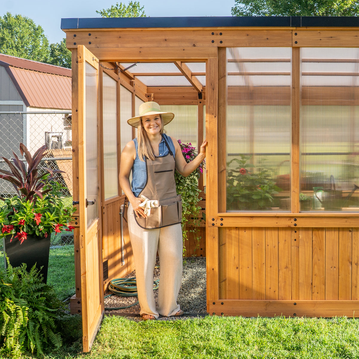 Woman gardening at the open year-round cedar greenhouse door with 4-wall polycarbonate panels.