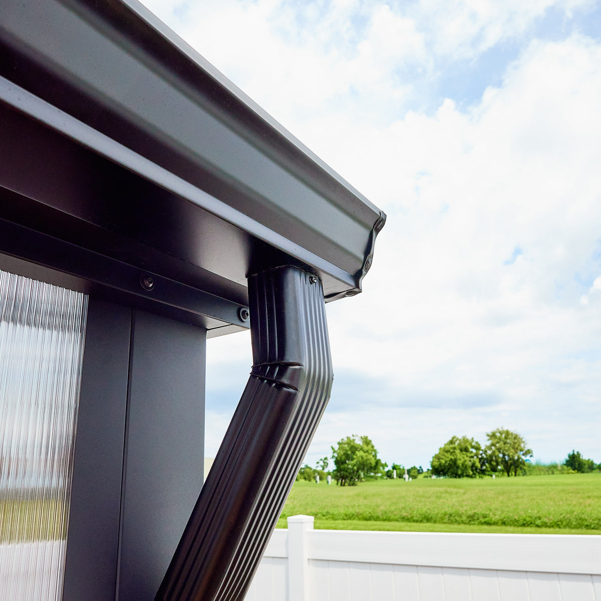 Gutter and downspout on a powder-coated steel greenhouse frame corner with 4-wall polycarbonate panels.