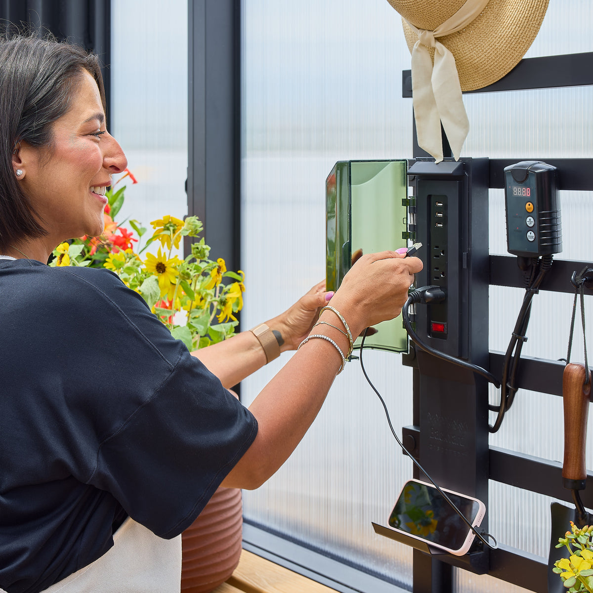 Woman plugging an USB cable into a PowerPort hub mounted on a powder-coated steel greenhouse slat wall.