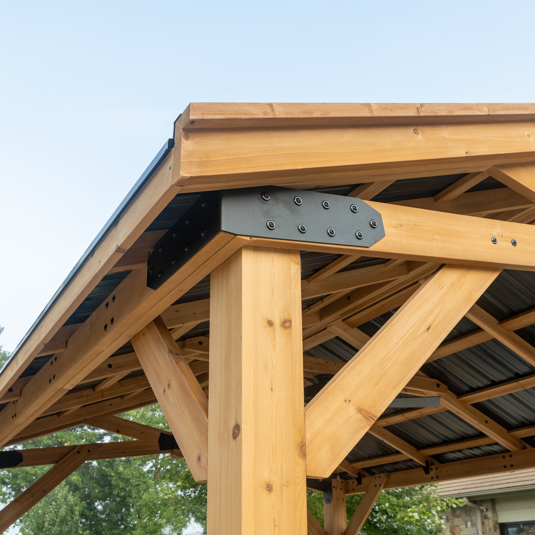 Corner bracket detail of steel gazebo showing metal connector joining cedar beams and roofing panels.