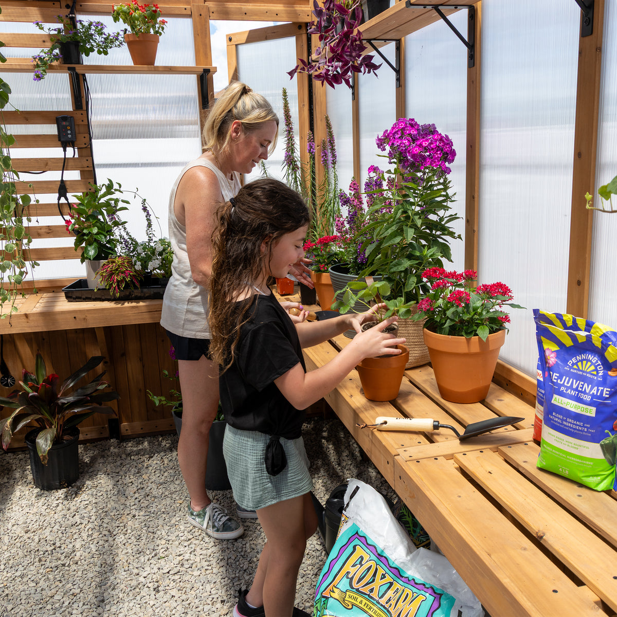 Woman and girl potting flowers on the staging shelves inside the Savannah cedar greenhouse.