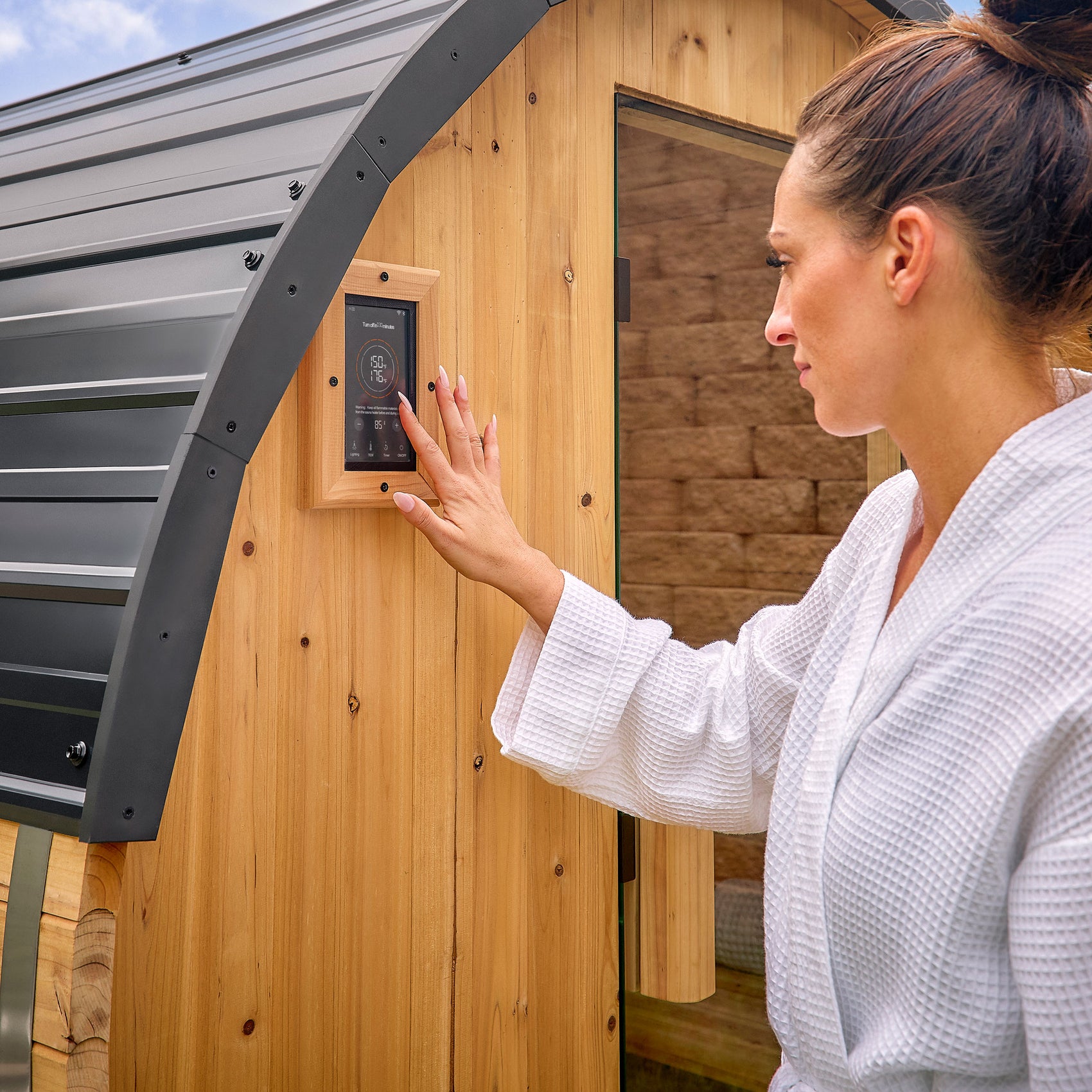 Woman adjusting digital temperature control panel on Paxton outdoor cedar barrel sauna