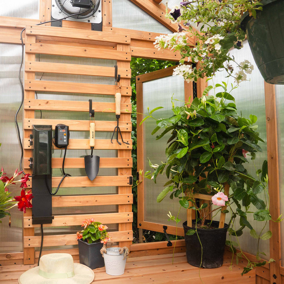 Slat wall organizer with garden tools, thermostat, and potted flowering plants.