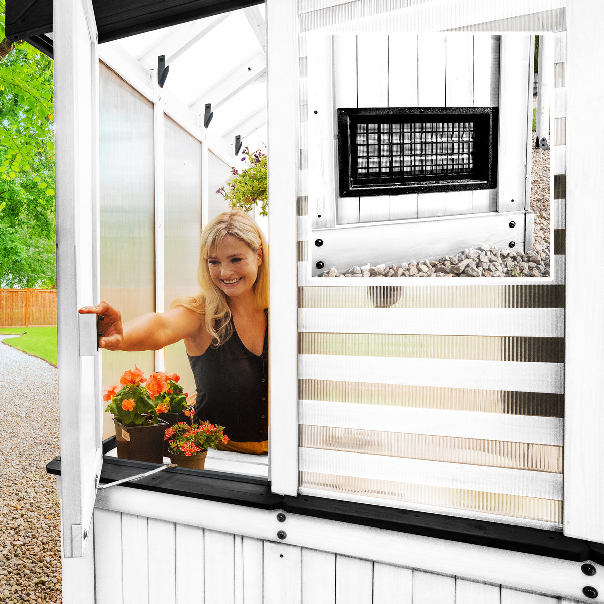 Woman opening an operable window on a DIY white-frame greenhouse for passive ventilation.