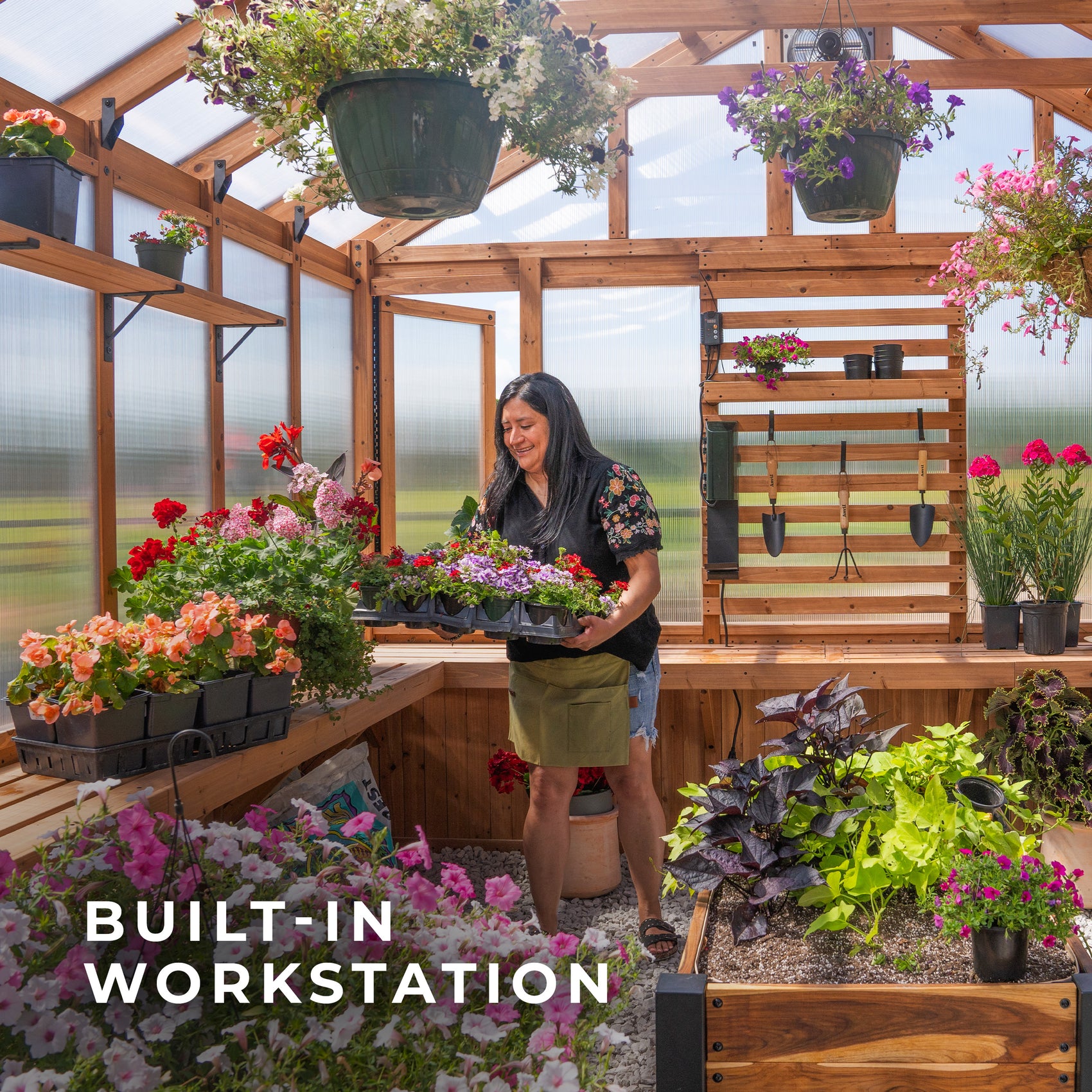 Woman arranging flower trays at the built-in workstation inside the Bellerose XL cedar greenhouse.