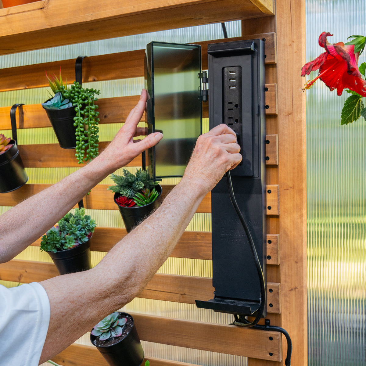 PowerPort hub being opened by a person on a cedar slat wall inside an outdoor greenhouse.