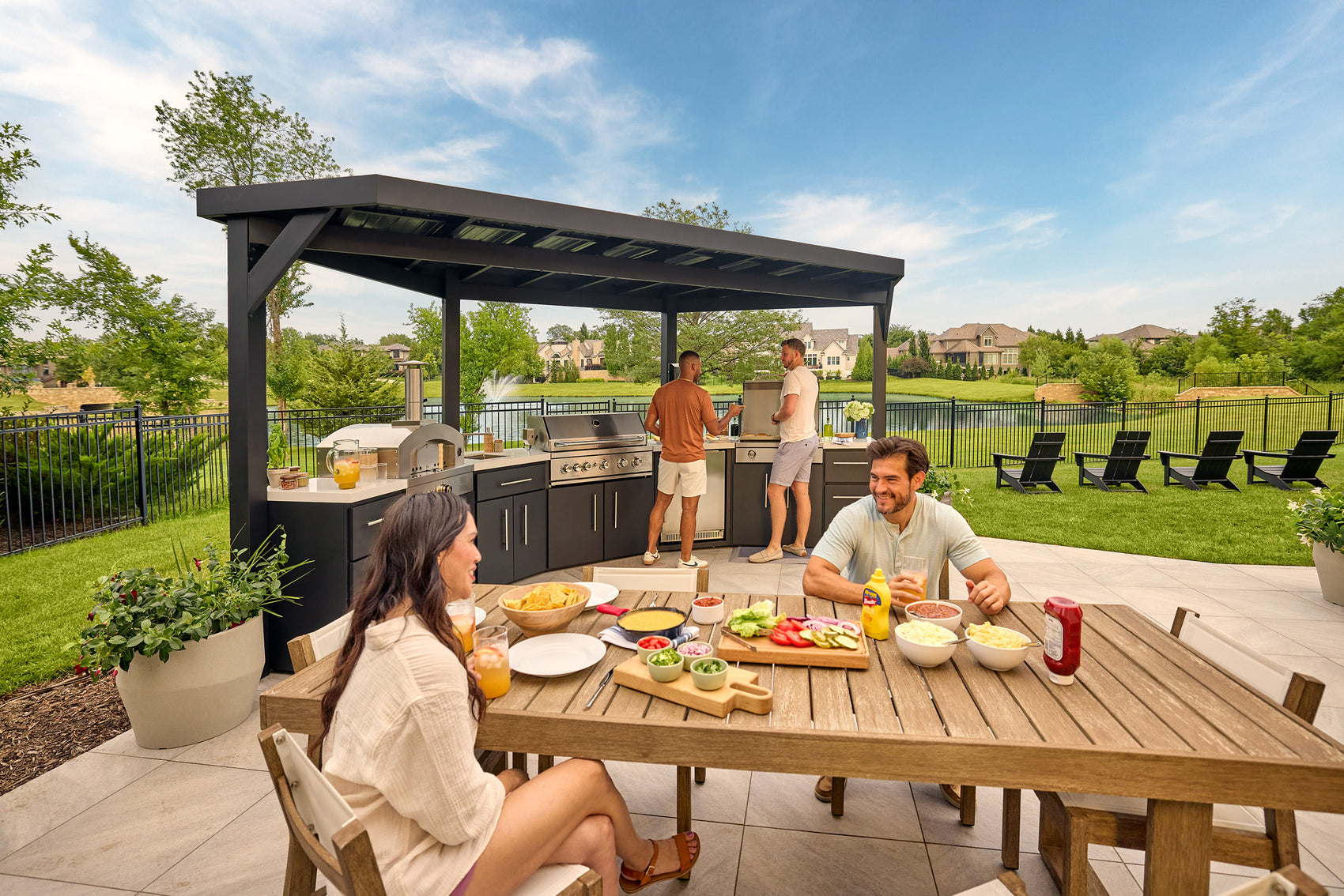 Edgemont Cove Outdoor Kitchen stainless steel under-counter refrigerator with door open, shelves fully stocked with canned beverages and food containers