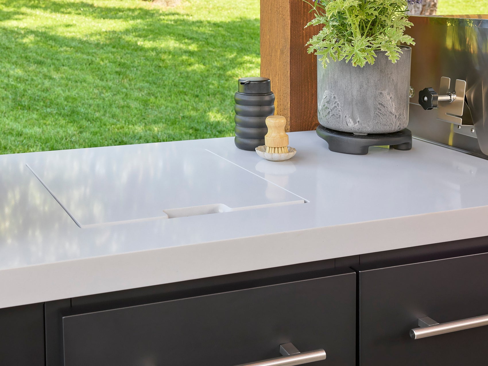 Covered bar sink with stowaway design in white engineered stone countertop with brush and soap dispenser.