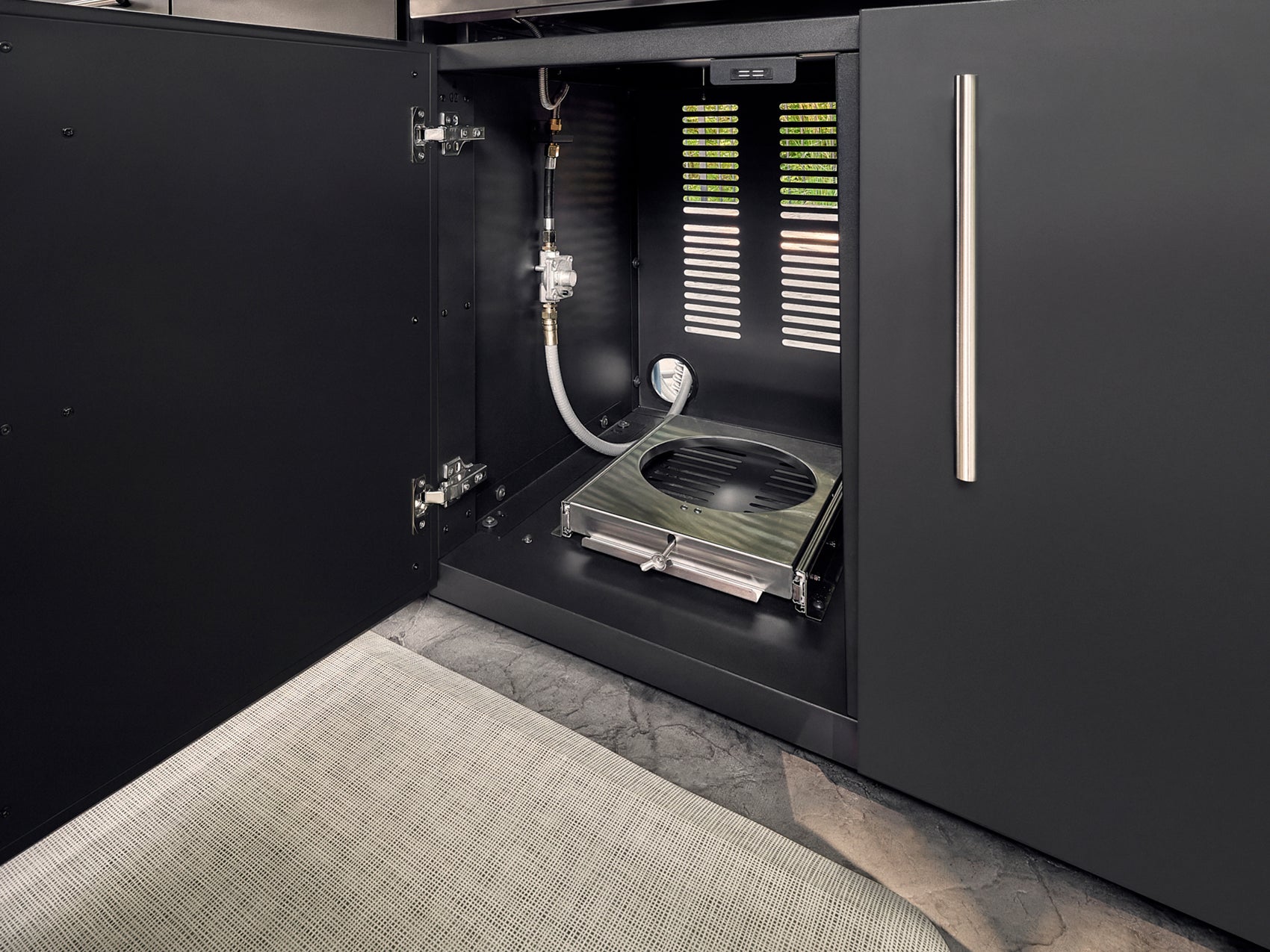 Built-in outdoor gas grill installed in black cabinetry with vented panel and flexible gas line connection.