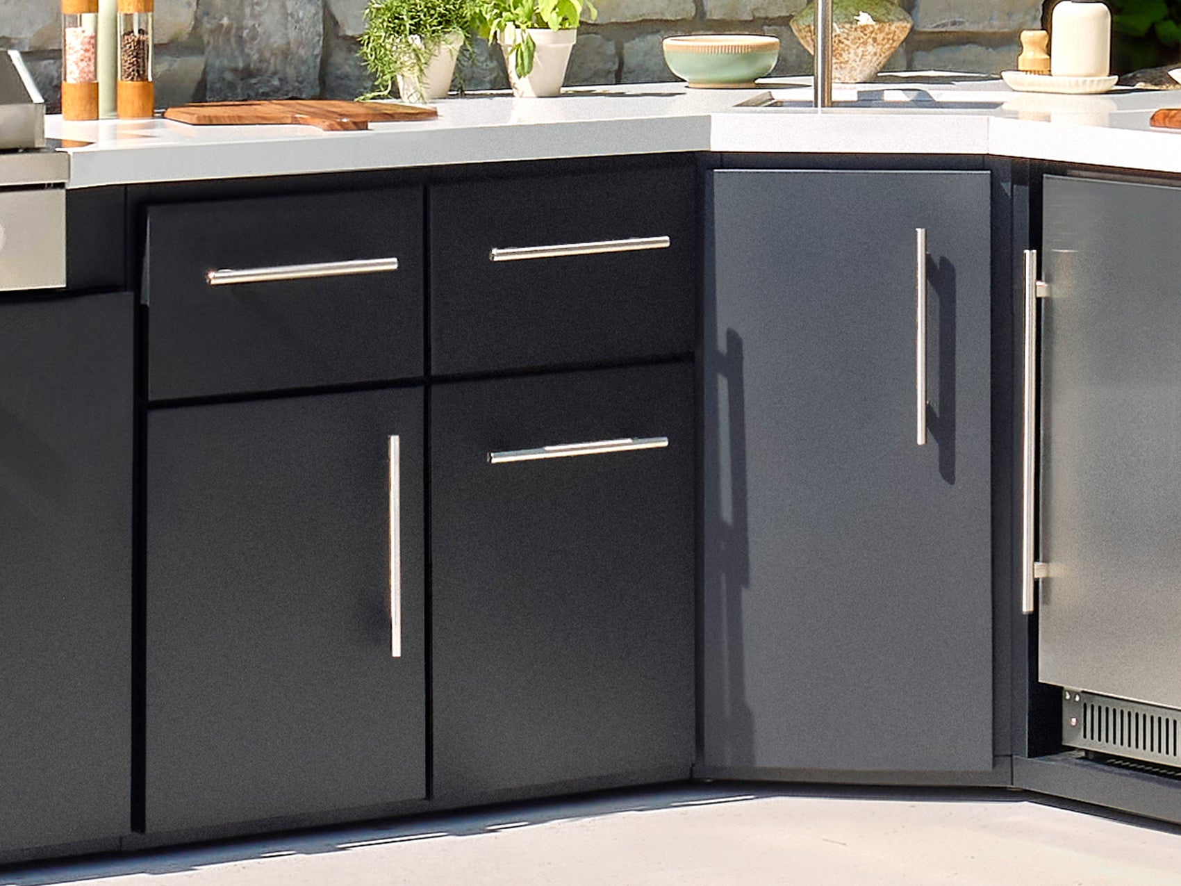 Emory black outdoor kitchen cabinets with silver bar pulls and white countertop for modern backyard design.