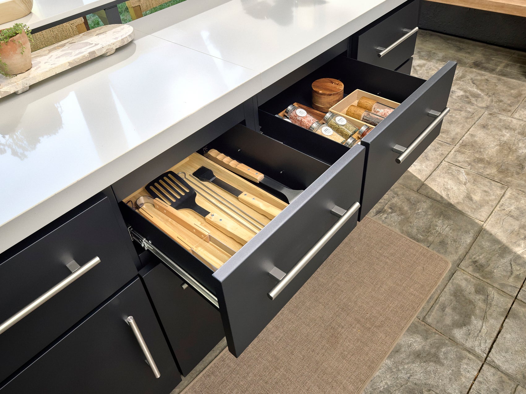 Open Emory outdoor cabinet drawers with bamboo utensil divider and spice organizer under white engineered stone countertop.