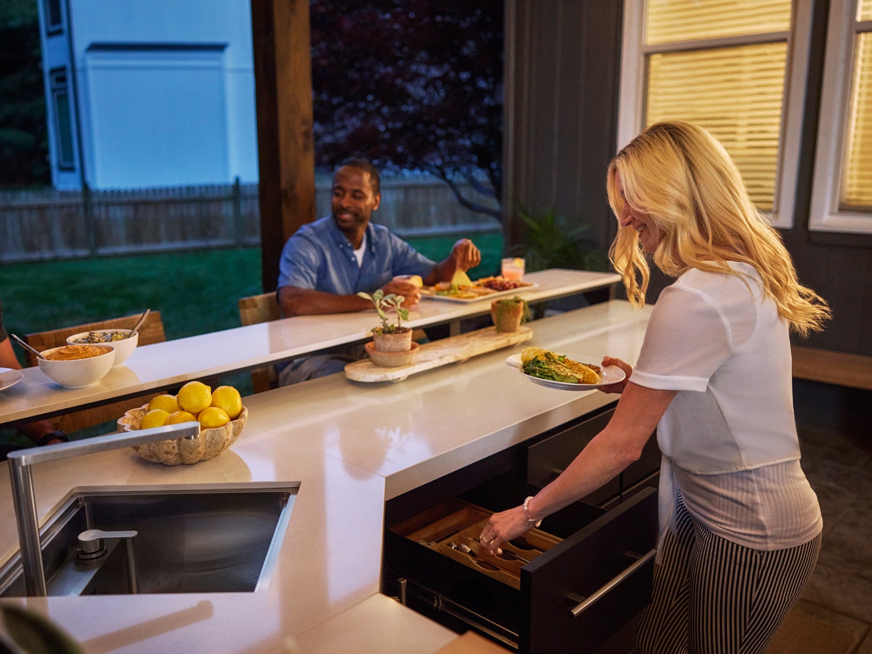 Range Outdoor Living Emory kitchen island where woman serves dinner as man dines at counter.