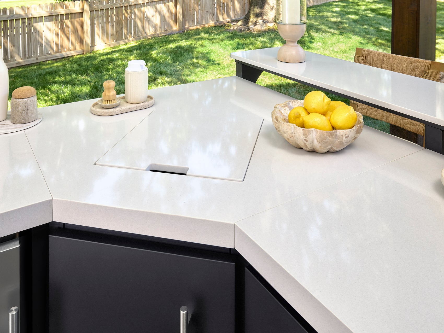 Outdoor sink station with sliding cover on engineered stone countertop with bowl of lemons and Emory kitchen accessories.
